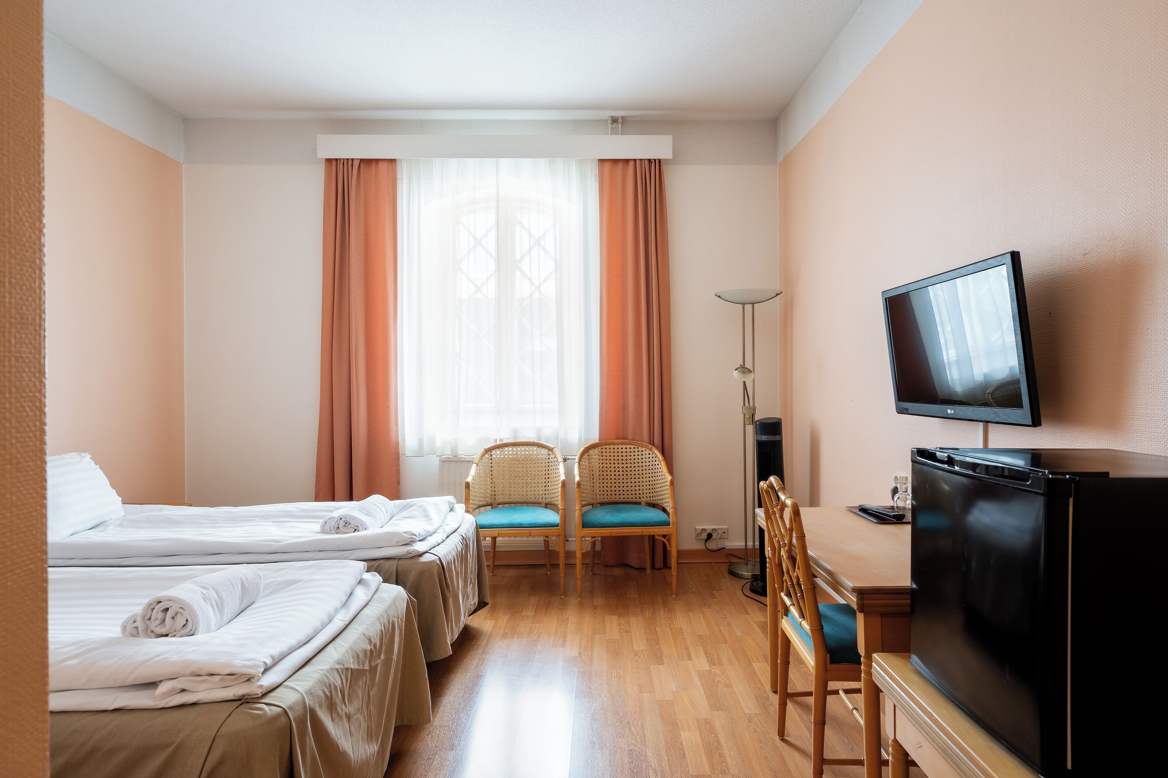 Ein Hotelzimmer mit zwei Betten, einem Fernseher, einem Schreibtisch und einem Sessel.