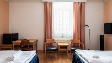 Habitación de hotel con dos camas, un escritorio con silla, televisión y ventana con cortinas.