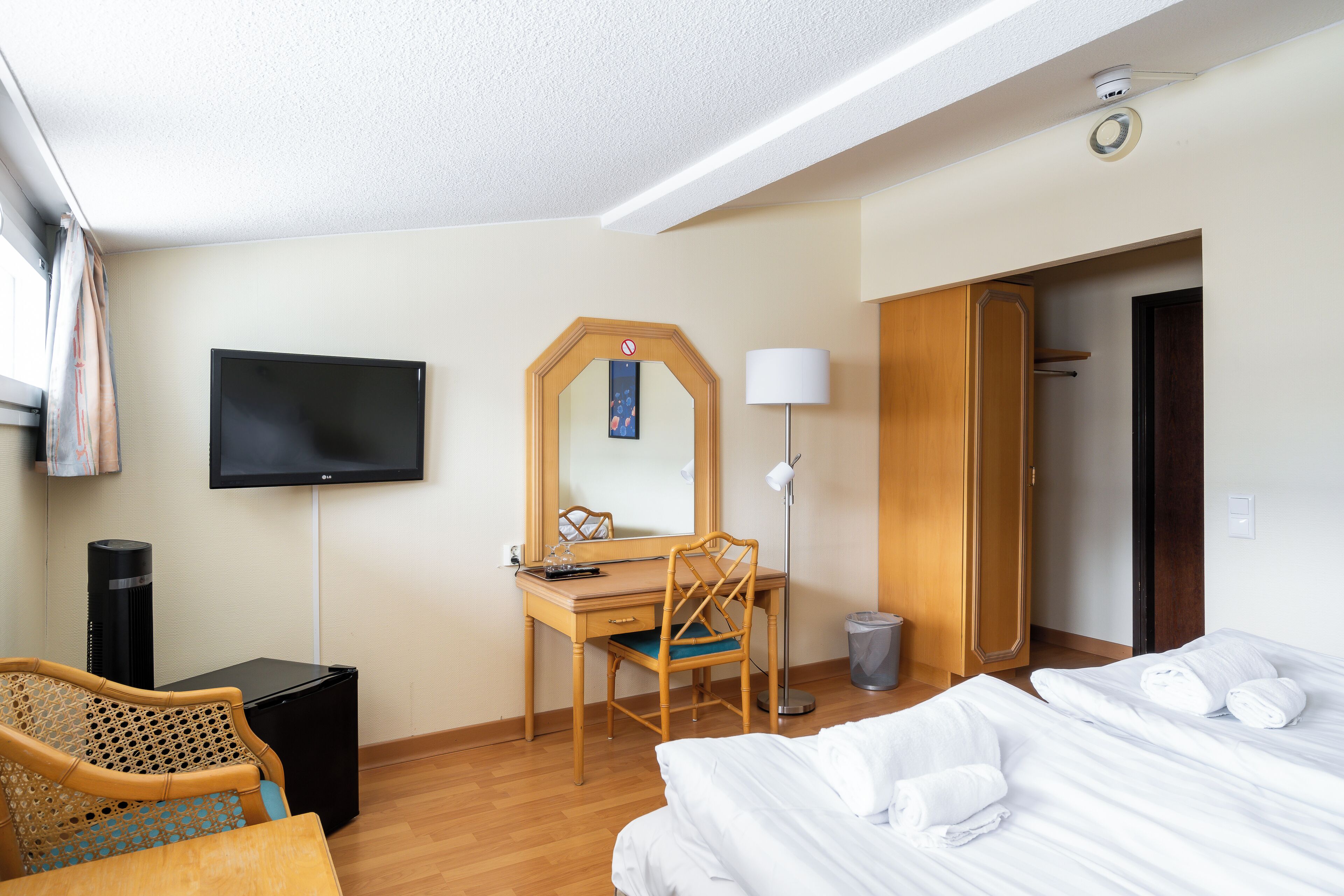 A hotel room with a bed, a desk, a chair, a television, and a wardrobe.