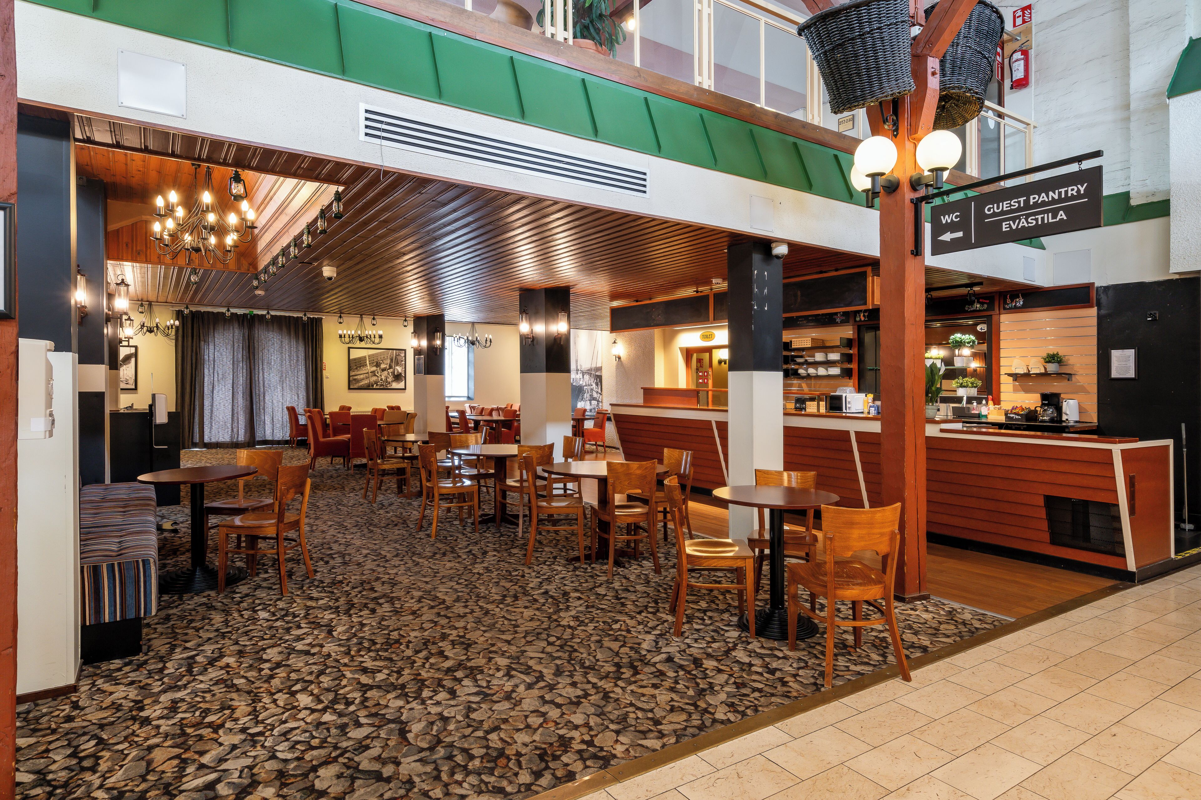 Un hall d’hôtel avec un sol carrelé en pierre, des meubles en bois et un panneau indiquant l’emplacement du garde-manger pour les clients.