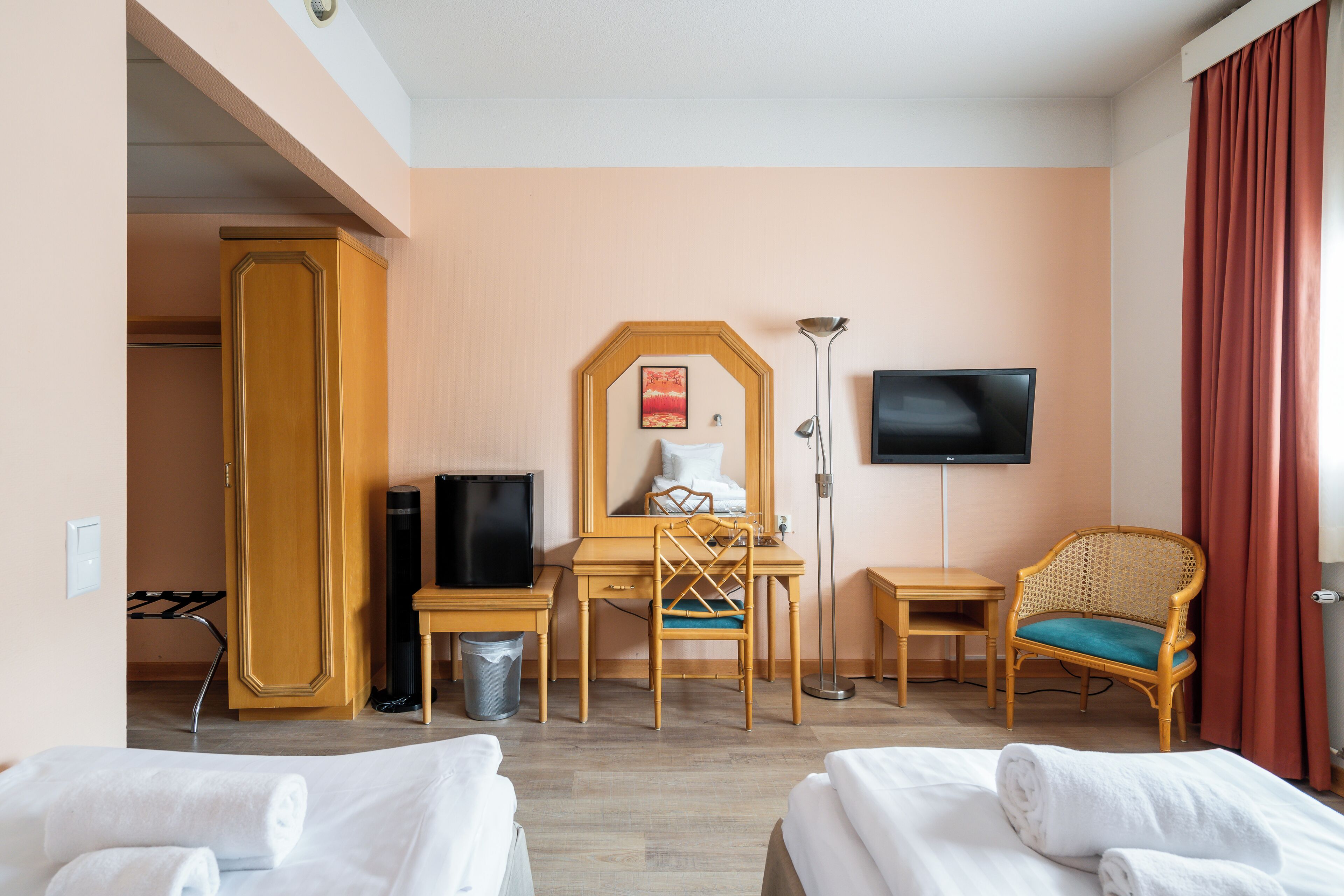 Habitación de hotel con dos camas, un escritorio, una silla, un televisor y un armario.