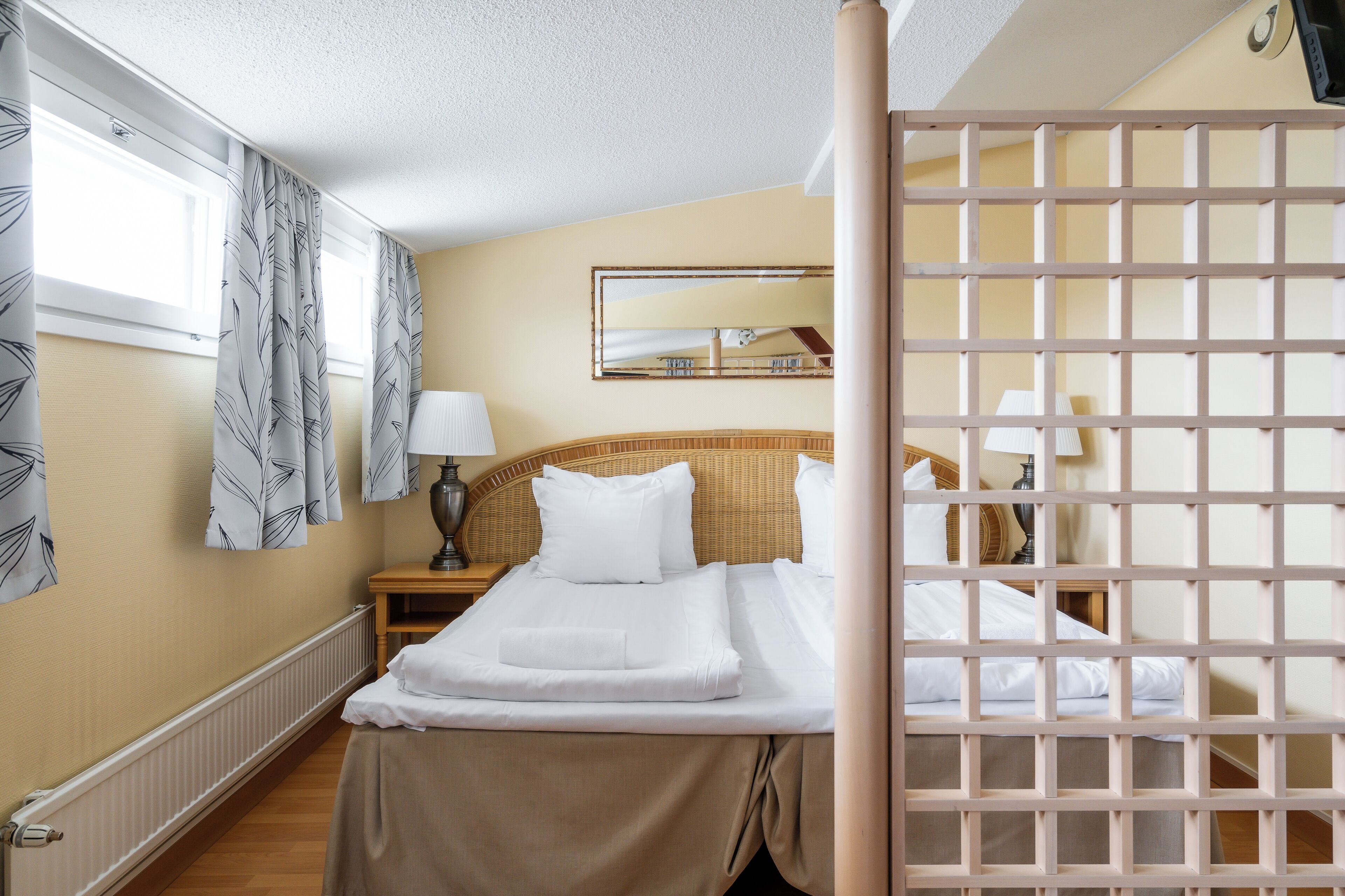 A hotel room with two beds, a large mirror, a nightstand, and a window with curtains.