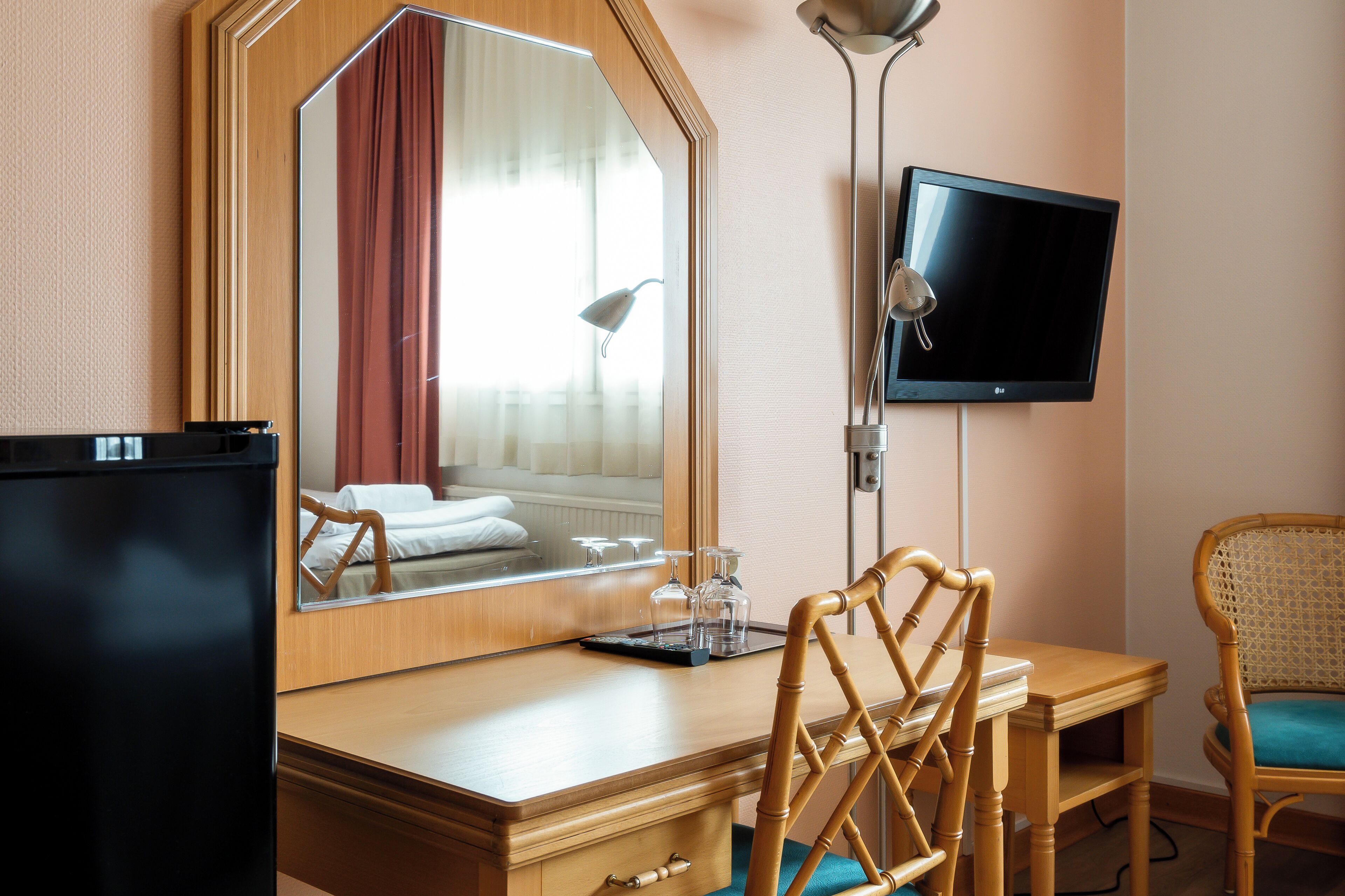 Habitación de hotel con escritorio de madera, televisor montado en la pared, espejo y cama con ventana.