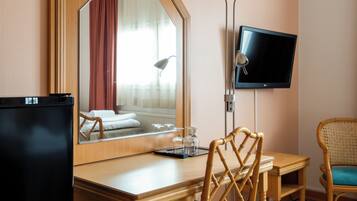 Habitación de hotel con escritorio de madera, televisor montado en la pared, espejo y cama con ventana.
