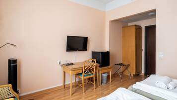 A hotel room with a wooden desk, a television, a chair, a bed with towels, and a trash bin.