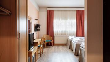 Habitación de hotel con escritorio de madera, televisión y cama con colcha blanca.