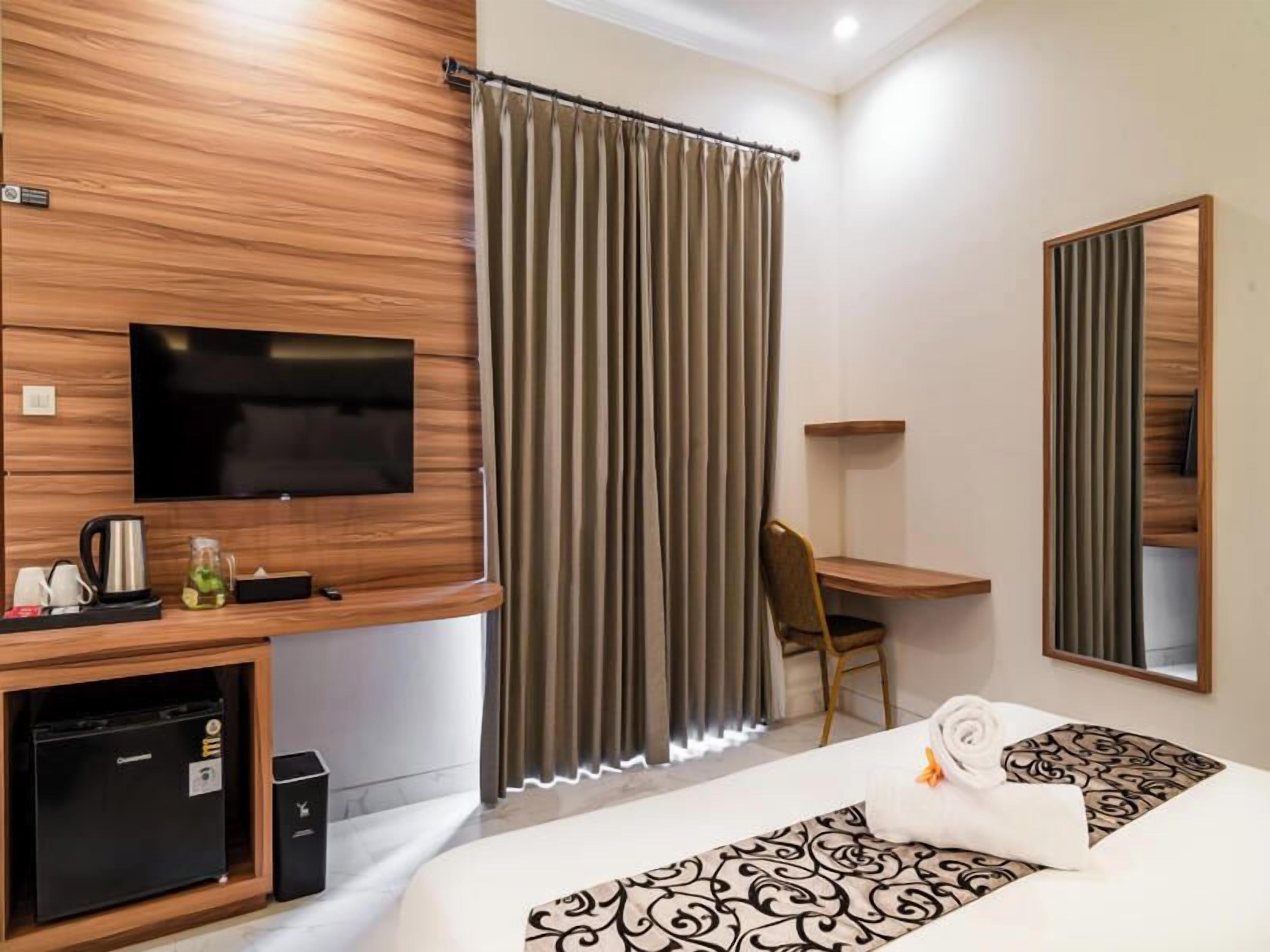 A hotel room with a bed, a desk, a TV, a minibar, and a large window with curtains.