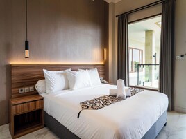 Habitación de hotel con una cama grande, una mesita de noche de madera, una lámpara colgante moderna y vistas al exterior a través de un ventanal amplio.