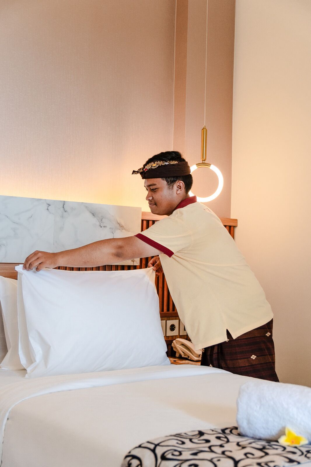 Una persona acomodando un almohadón blanco en una cama con cabecera de mármol.