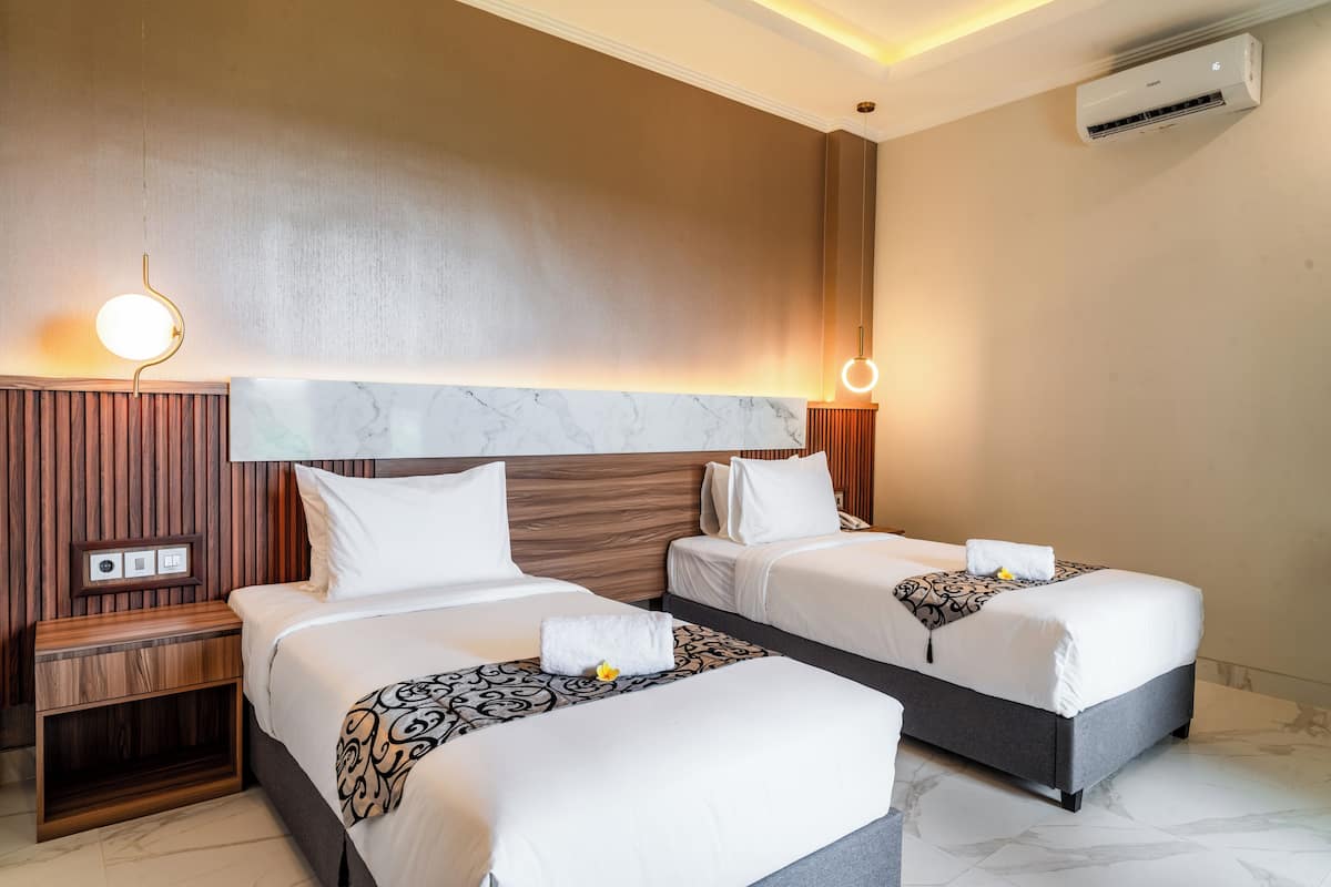 A hotel room with two beds, a wooden nightstand, a marble headboard, and an air conditioning unit.