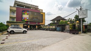 Ingresso di un hotel con viale lastricato, auto parcheggiate e area riservata a motocicli.