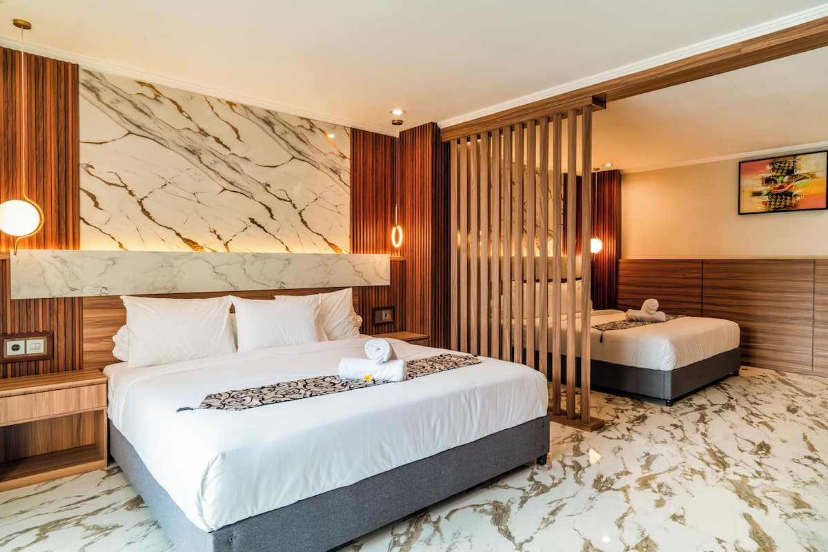 A modern hotel room with a large bed, a wooden headboard, a marble-patterned wall, and a wooden partition.
