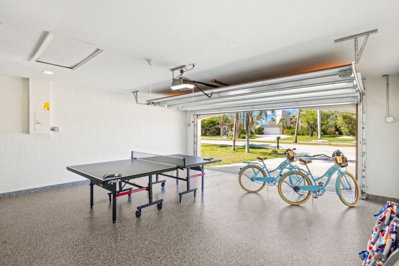 Ein Zimmer mit Tischtennisplatte, einem Fahrrad und Blick auf einen Park durch ein großes Fenster.