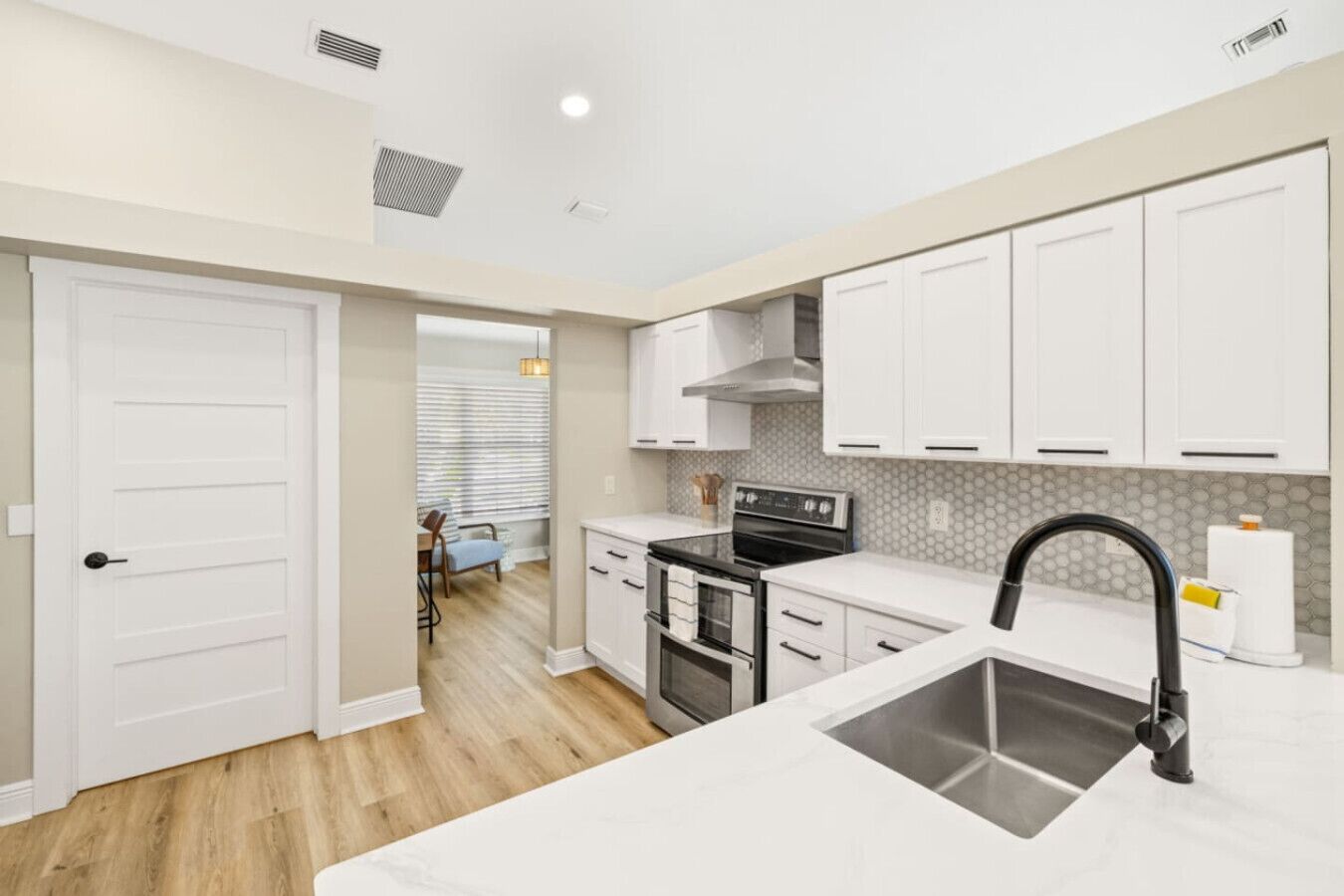A modern kitchen with white cabinets, a stainless steel sink, and a black faucet.