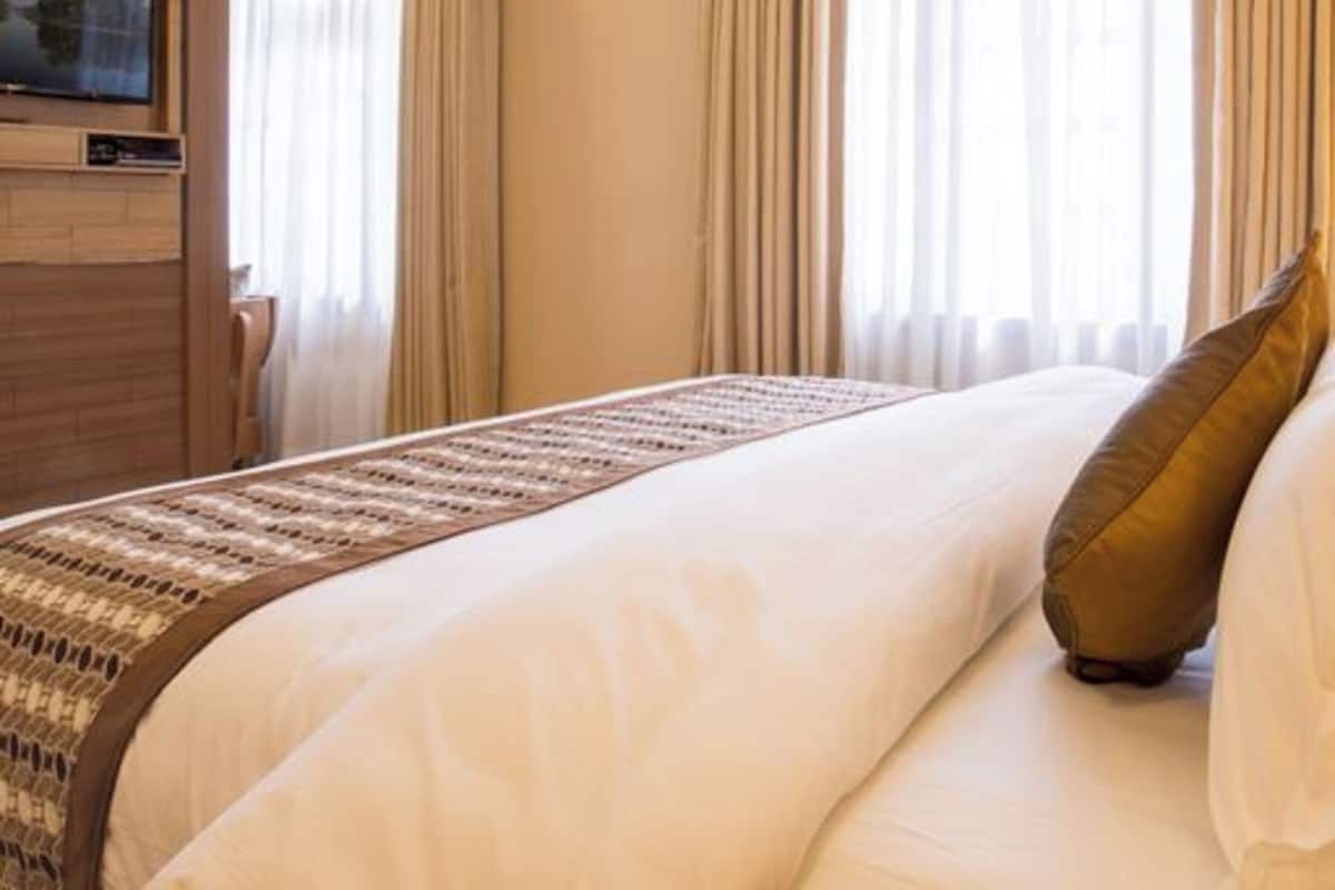 A hotel room with a large bed, a television mounted on the wall, and a window with curtains.