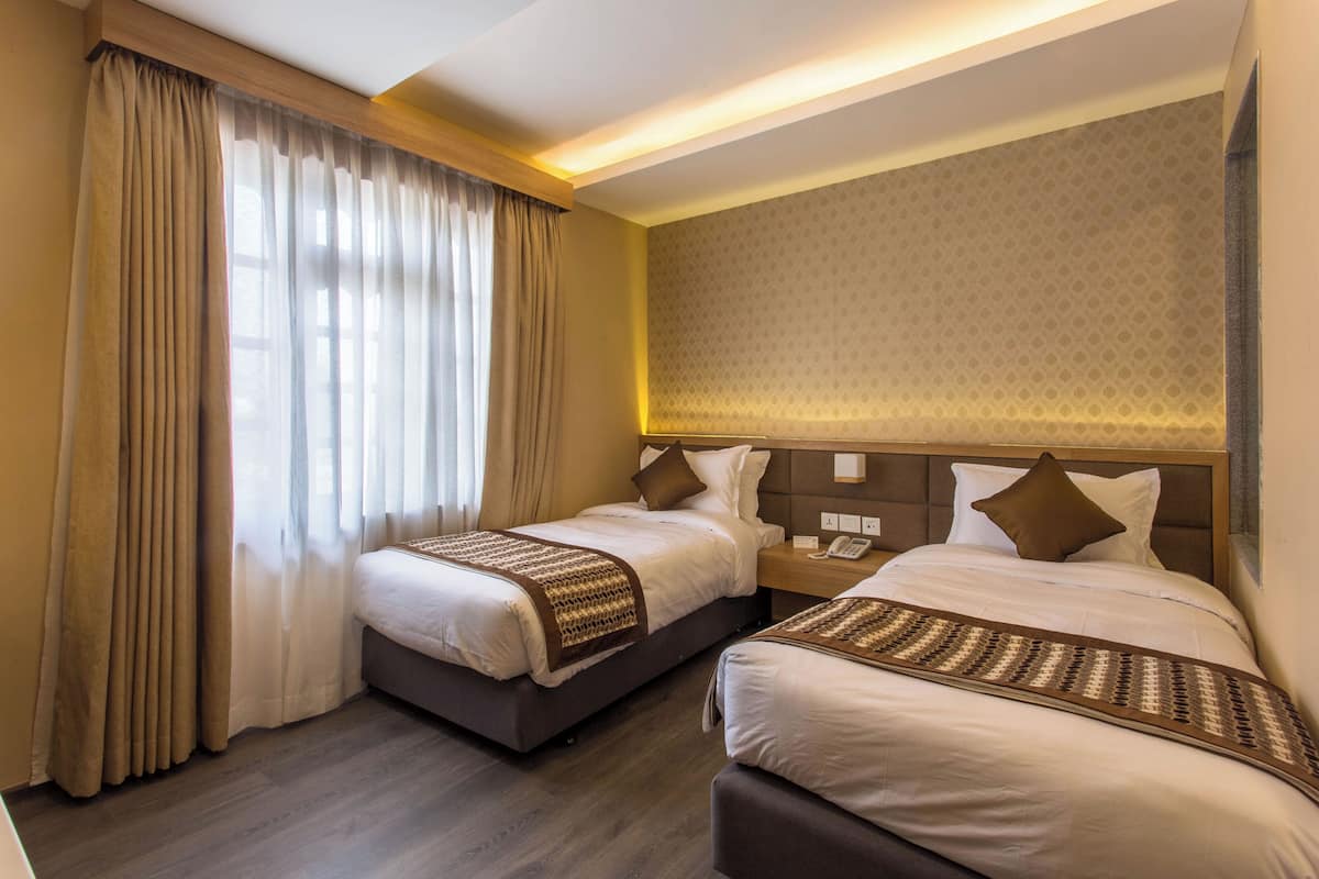 A hotel room with two beds, a large window with curtains, a patterned wall, and a nightstand with a phone.