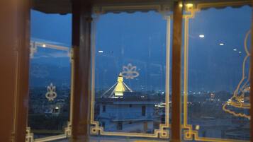 Vista a través de una ventana con un marco decorativo, que muestra un edificio con una torre iluminada y un paisaje urbano al fondo.