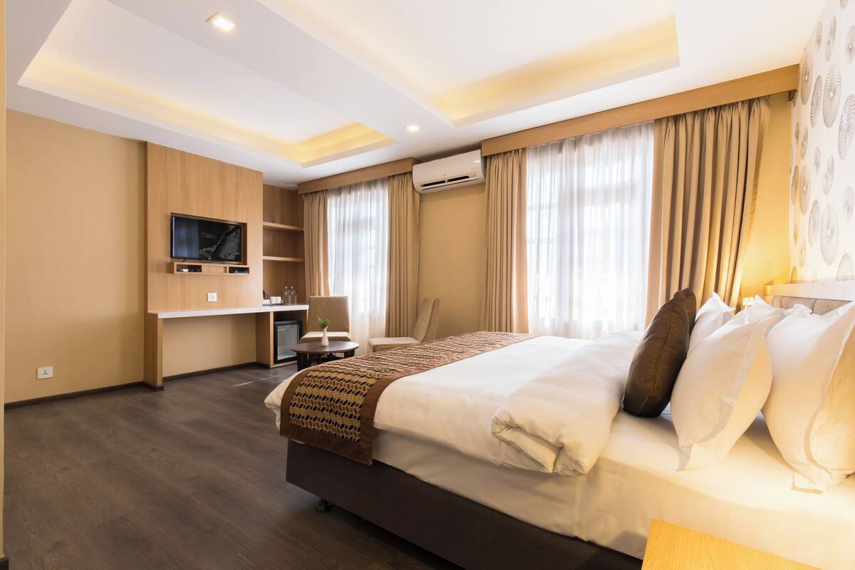 A modern hotel room with a large bed, a flat-screen TV, a desk, and a comfortable seating area.