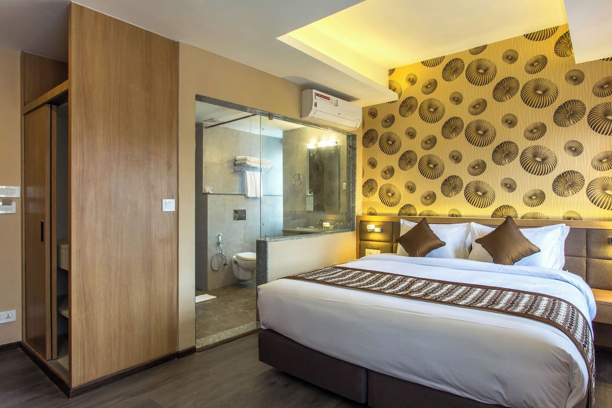 A hotel room with a large bed, a glass-enclosed shower, a wooden wardrobe, and a patterned wall.