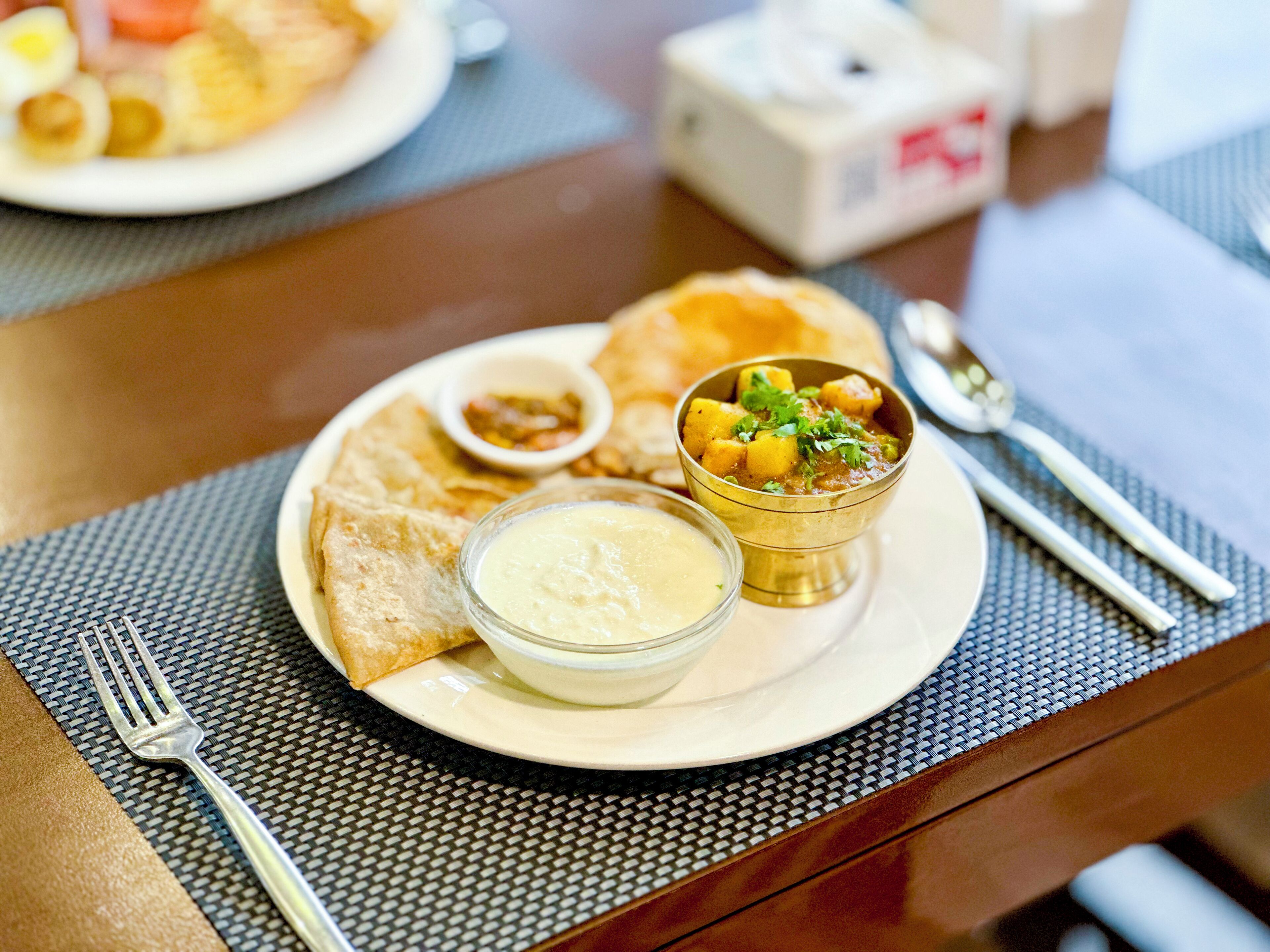 A plate with food, a bowl, and a spoon on a table.