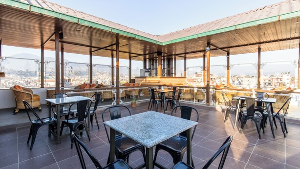 Una terraza en la azotea con mobiliario exterior, zona de bar y vistas panorámicas de la ciudad.