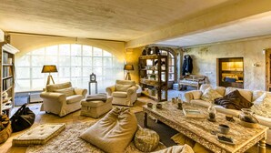 A spacious living room with a large arched window, a fireplace, and a bookshelf filled with books and decorative items. - Charming Charming Village House (AA+Wifi+Swimming Pool) (Riumors)