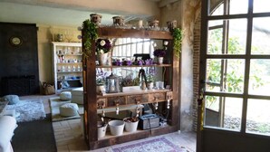 A rustic interior with a wooden shelf displaying various items, a fireplace, and a large window with a view of greenery. - Charming Charming Village House (AA+Wifi+Swimming Pool) (Riumors)