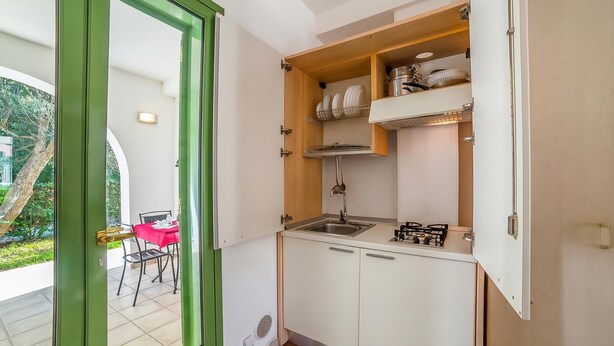 A compact kitchen with white cabinets, a stainless steel sink, and a gas stove. - Family Village T2 Pool And Sea (Otranto)