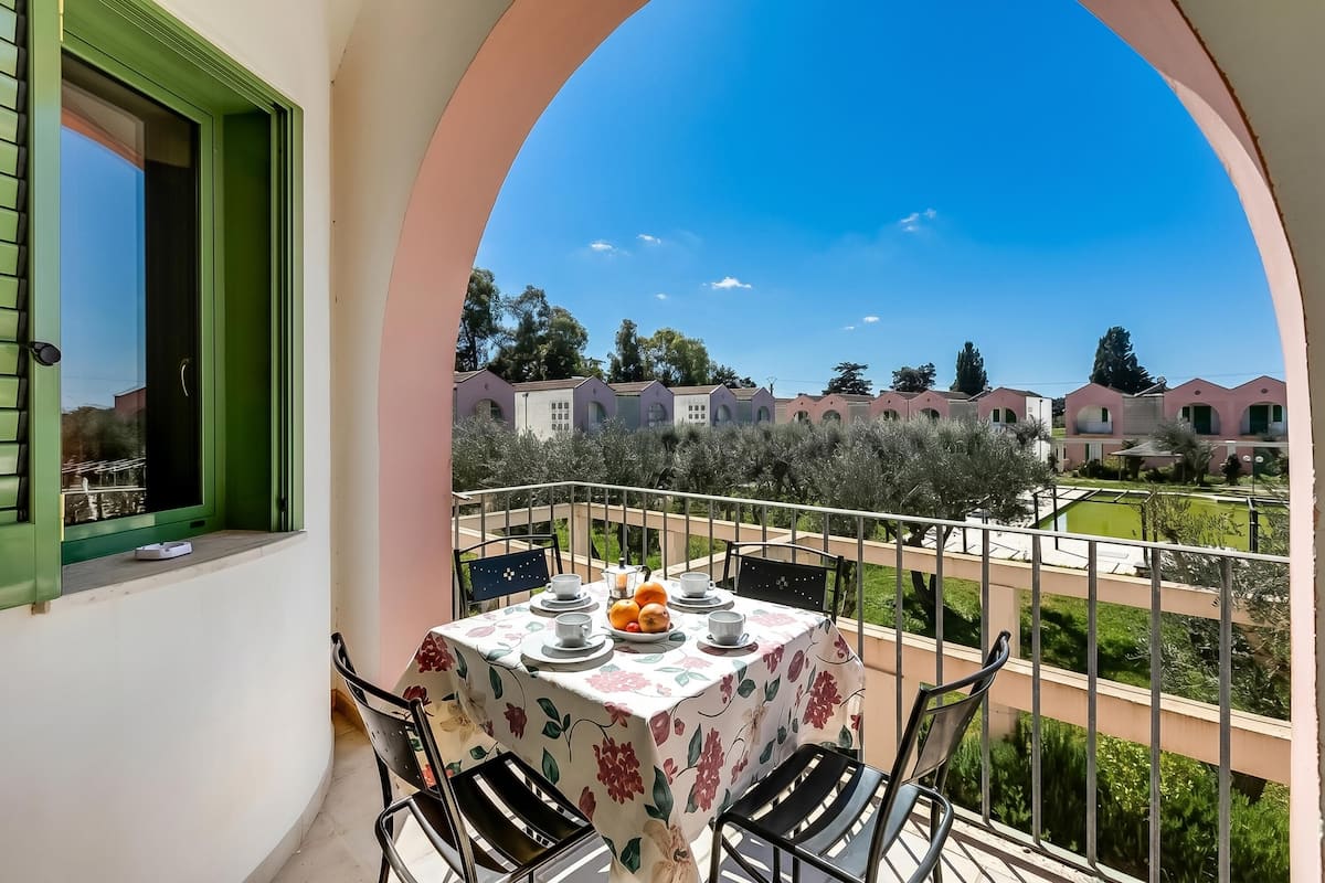 Un balcon avec une table dressée pour les repas, des chaises et une vue sur les bâtiments voisins.
