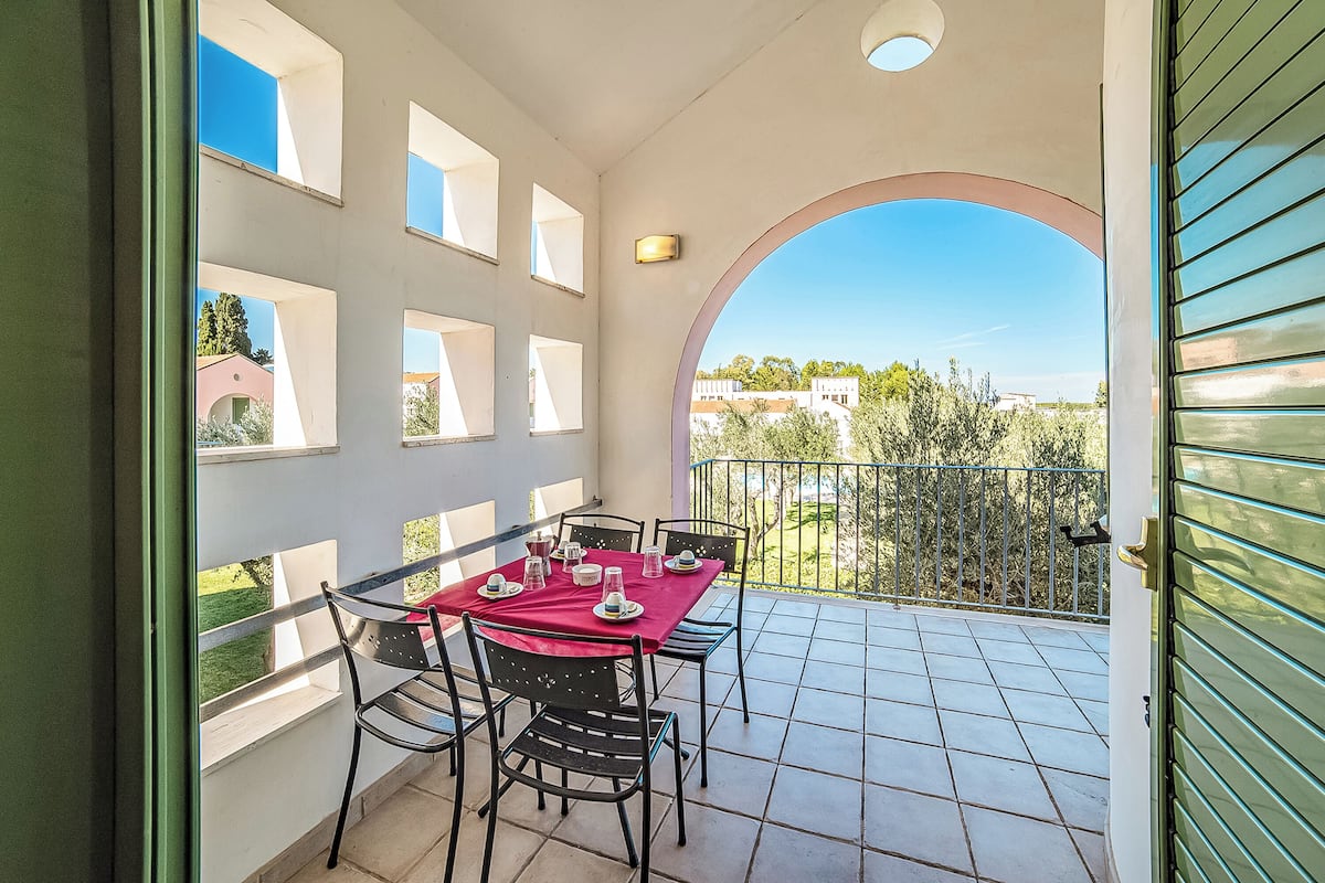 Un balcon avec une table dressée pour le dîner, agrémenté d’une nappe rouge et de chaises.