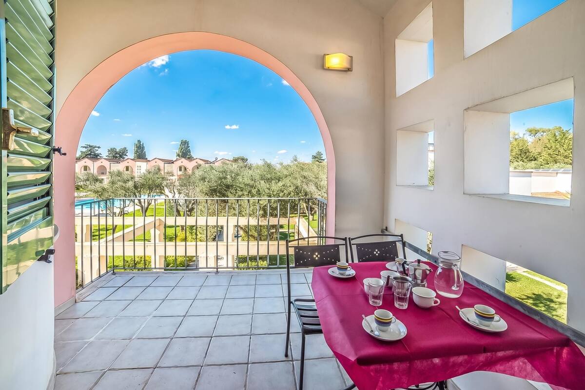 Un balcon avec une table préparée pour le thé, et une vue dégagée sur une piscine et des bâtiments en arrière-plan.