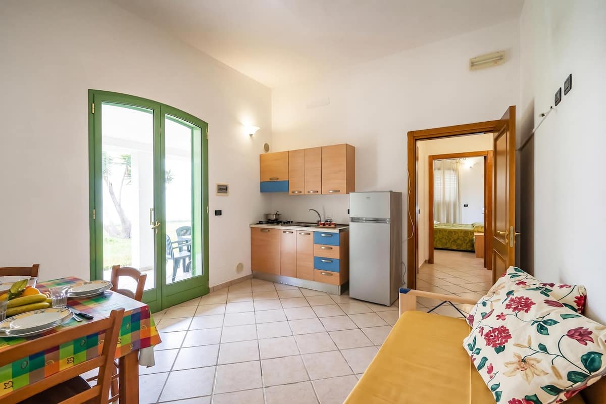 Une cuisine de taille réduite, équipée d’un réfrigérateur, de meubles en bois et d’un coin repas avec une table et des chaises.