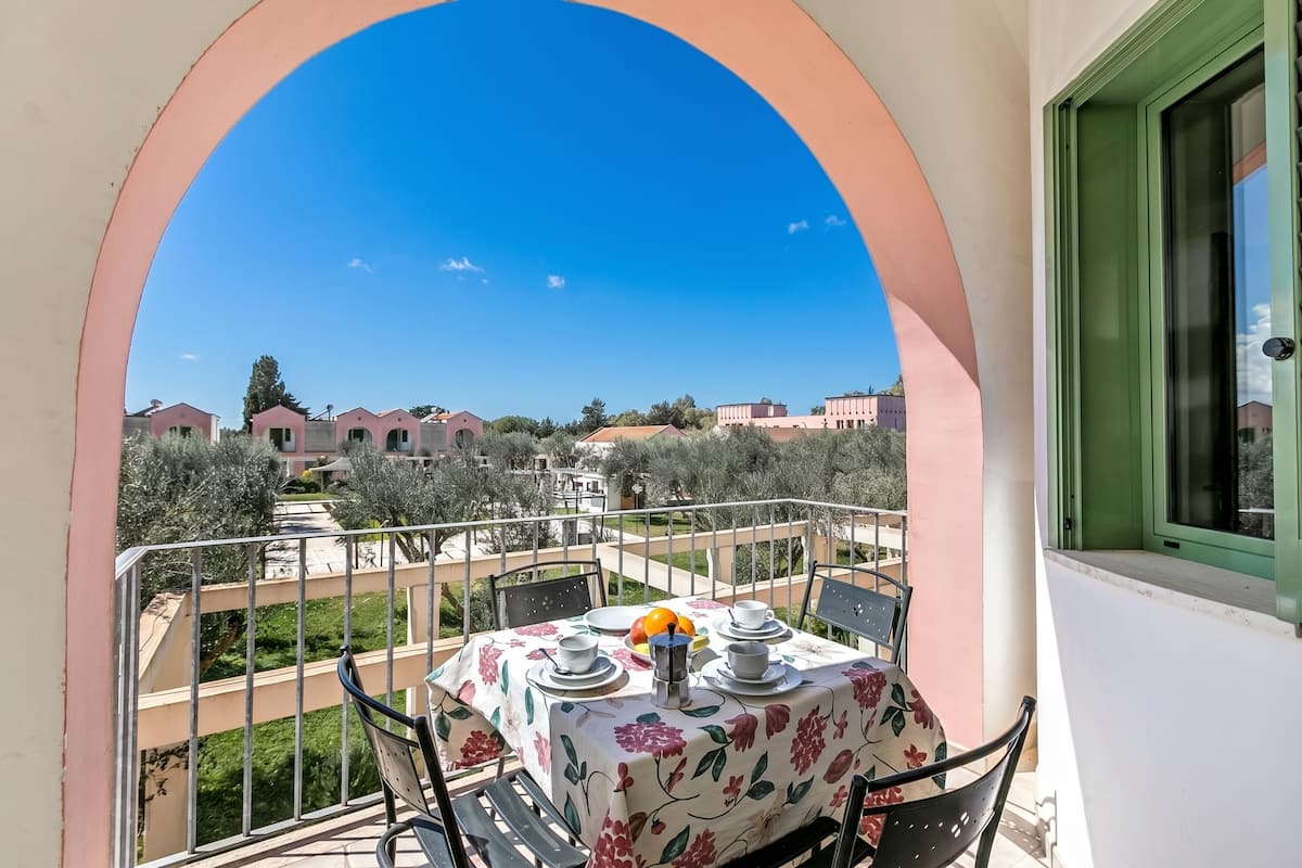 Un balcon avec une table dressée pour deux personnes, une vue sur les bâtiments environnants et un ciel bleu dégagé.