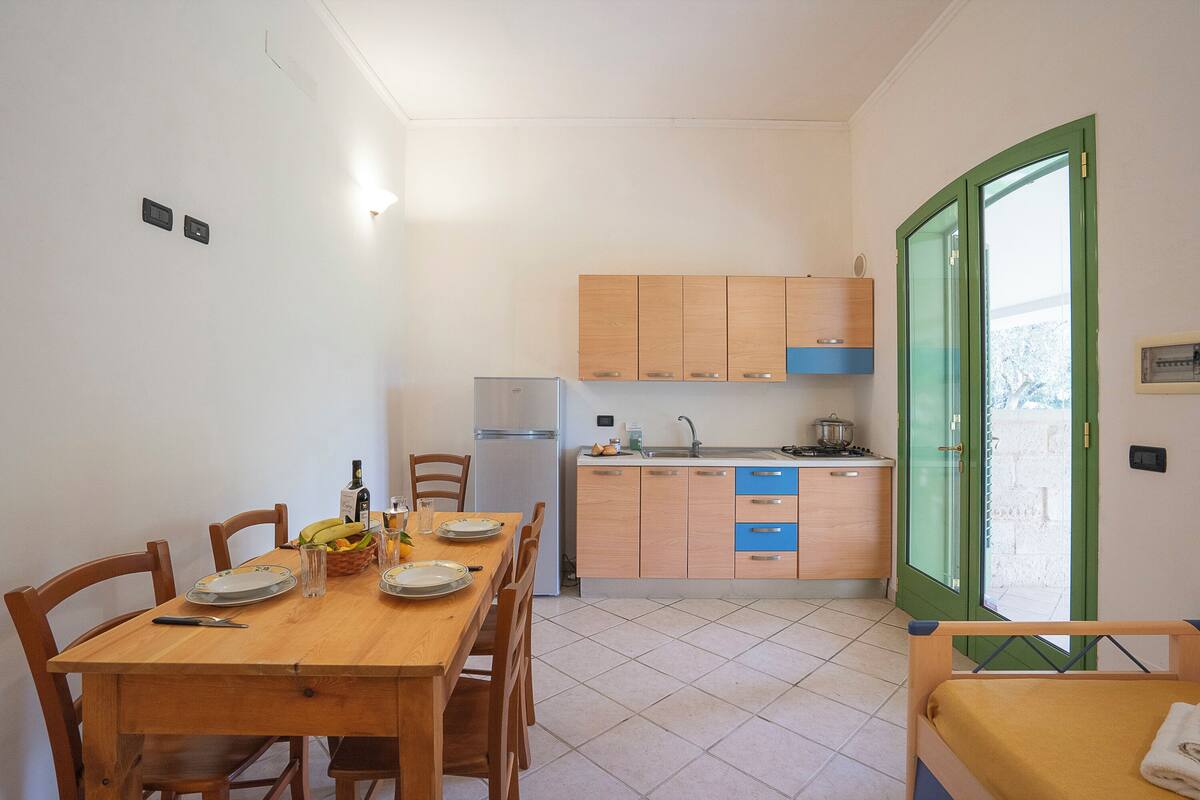 Une cuisine compacte avec des meubles de rangement en bois, une table à manger pour deux personnes et un petit réfrigérateur.