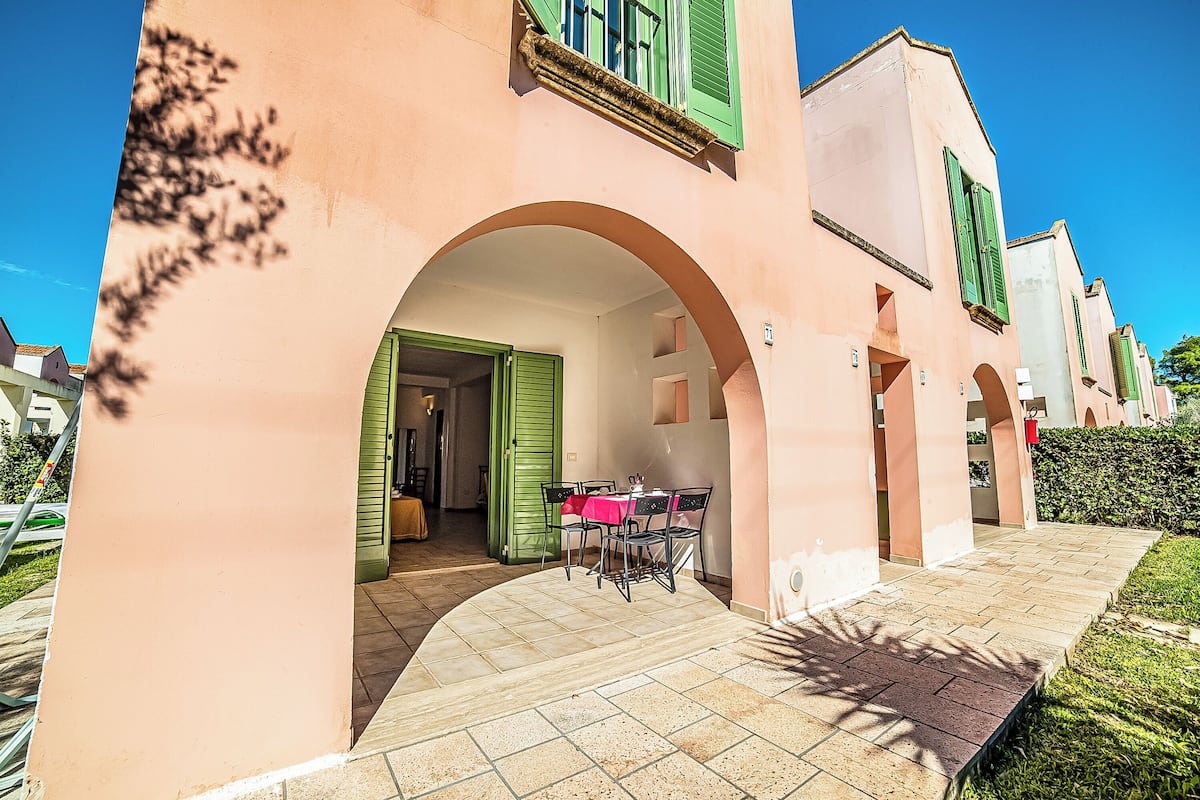 Un bâtiment à la façade rose, aux volets verts et doté d’un patio carrelé avec une table et des chaises.