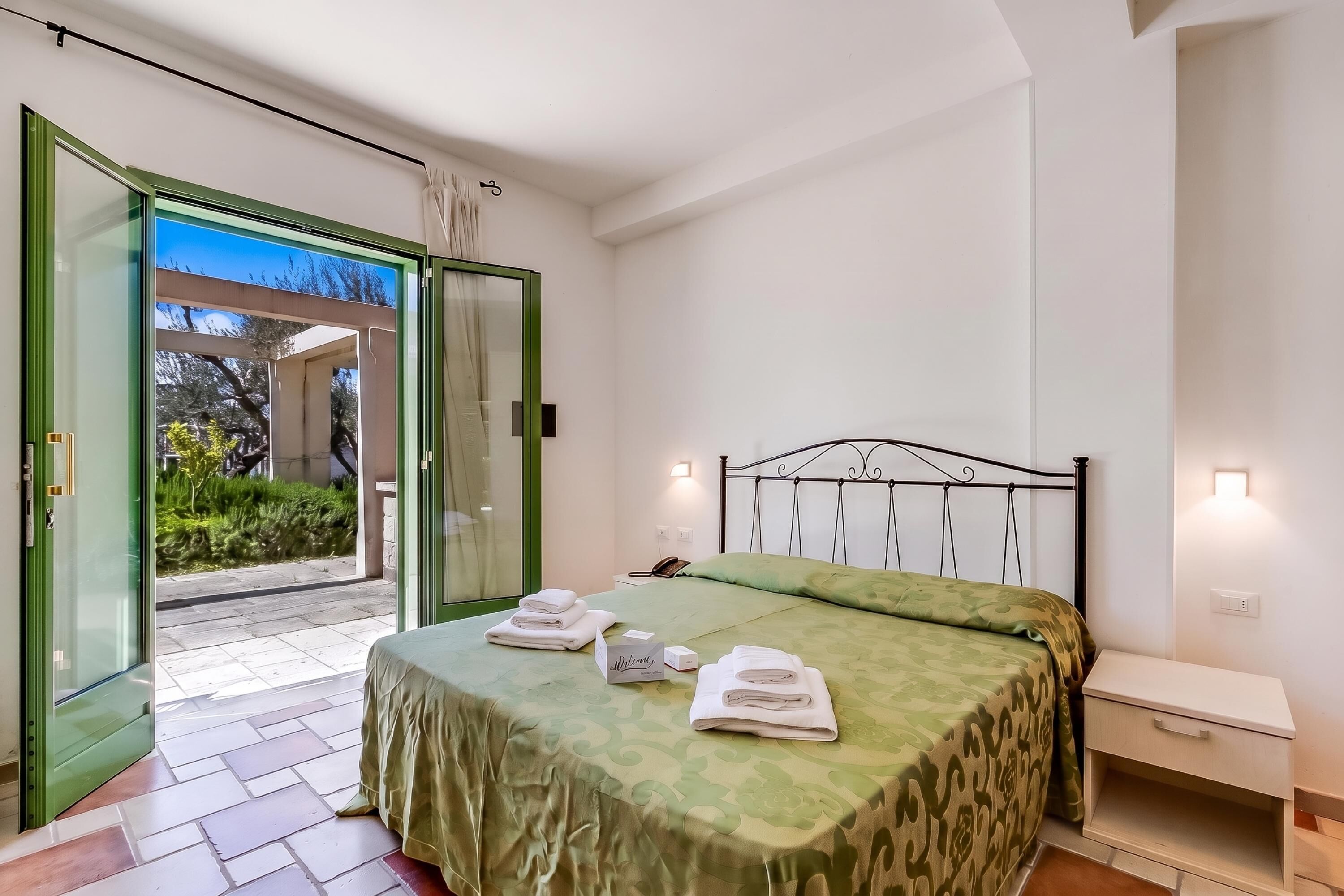 Une chambre d’hôtel avec un lit, une table de chevet, une commode et une vue à travers une porte vitrée.