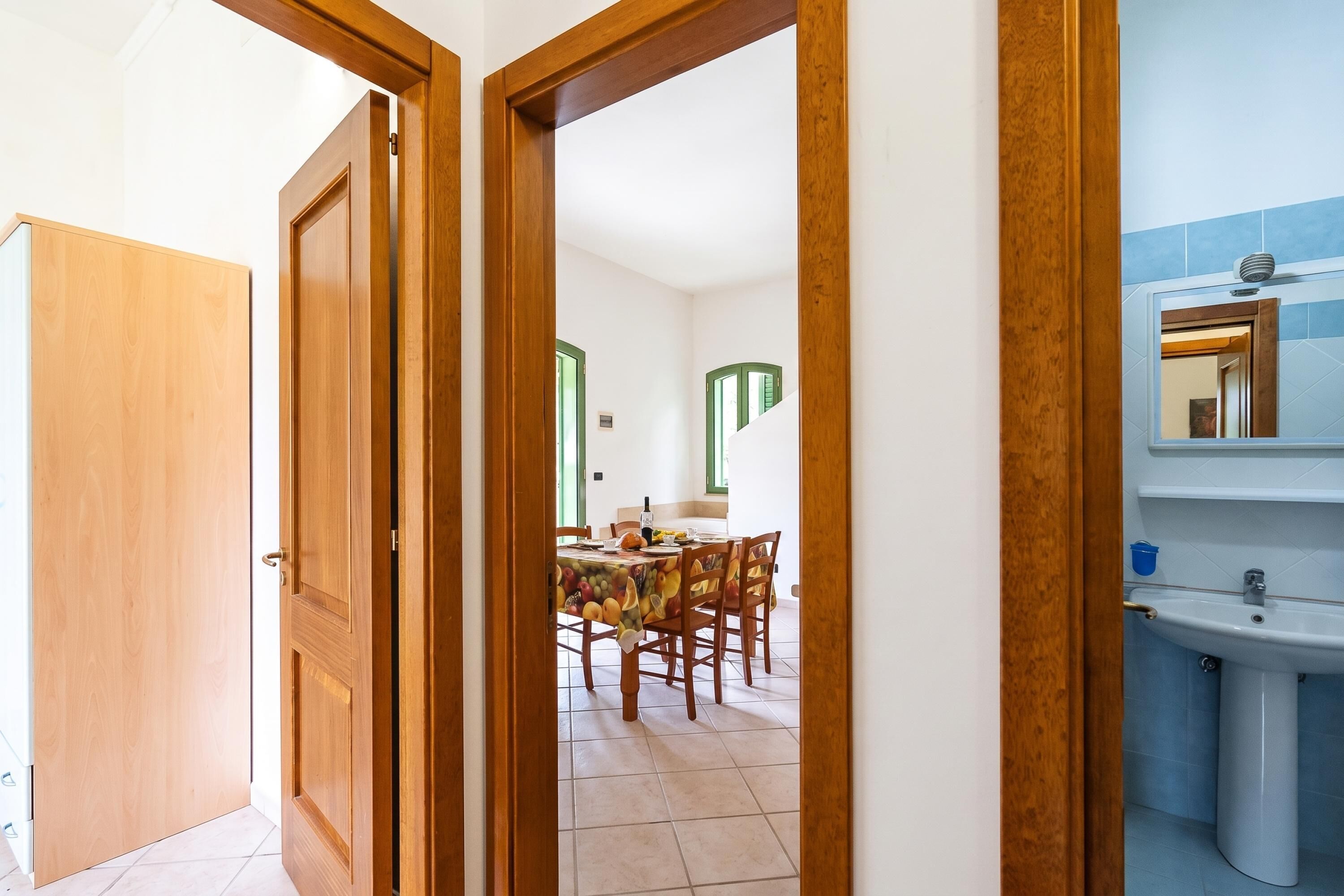 A room with a wooden door, a dining area with a table and chairs, and a bathroom with a sink and mirror.