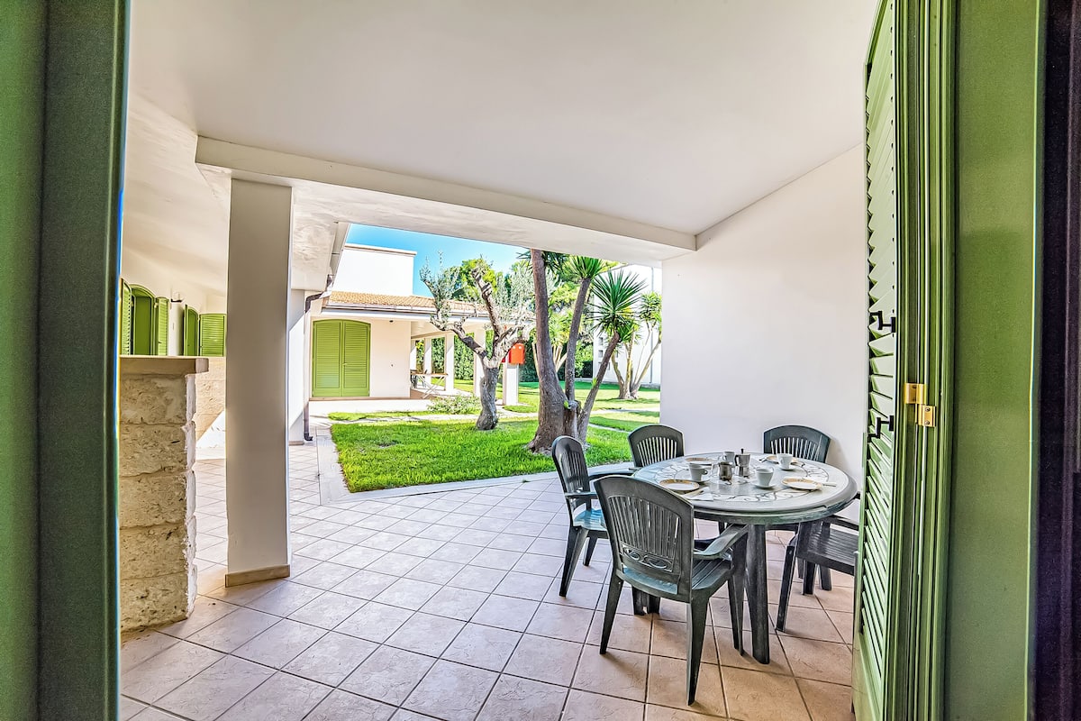 Une terrasse extérieure avec une table ronde et des chaises, un sol carrelé et une vue sur un immeuble et des arbres.
