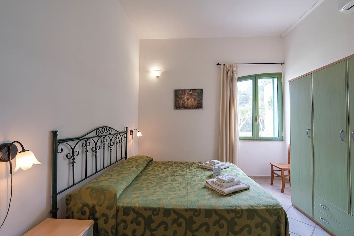 Une chambre à coucher avec un lit, une table de chevet, une armoire et une fenêtre avec des rideaux.