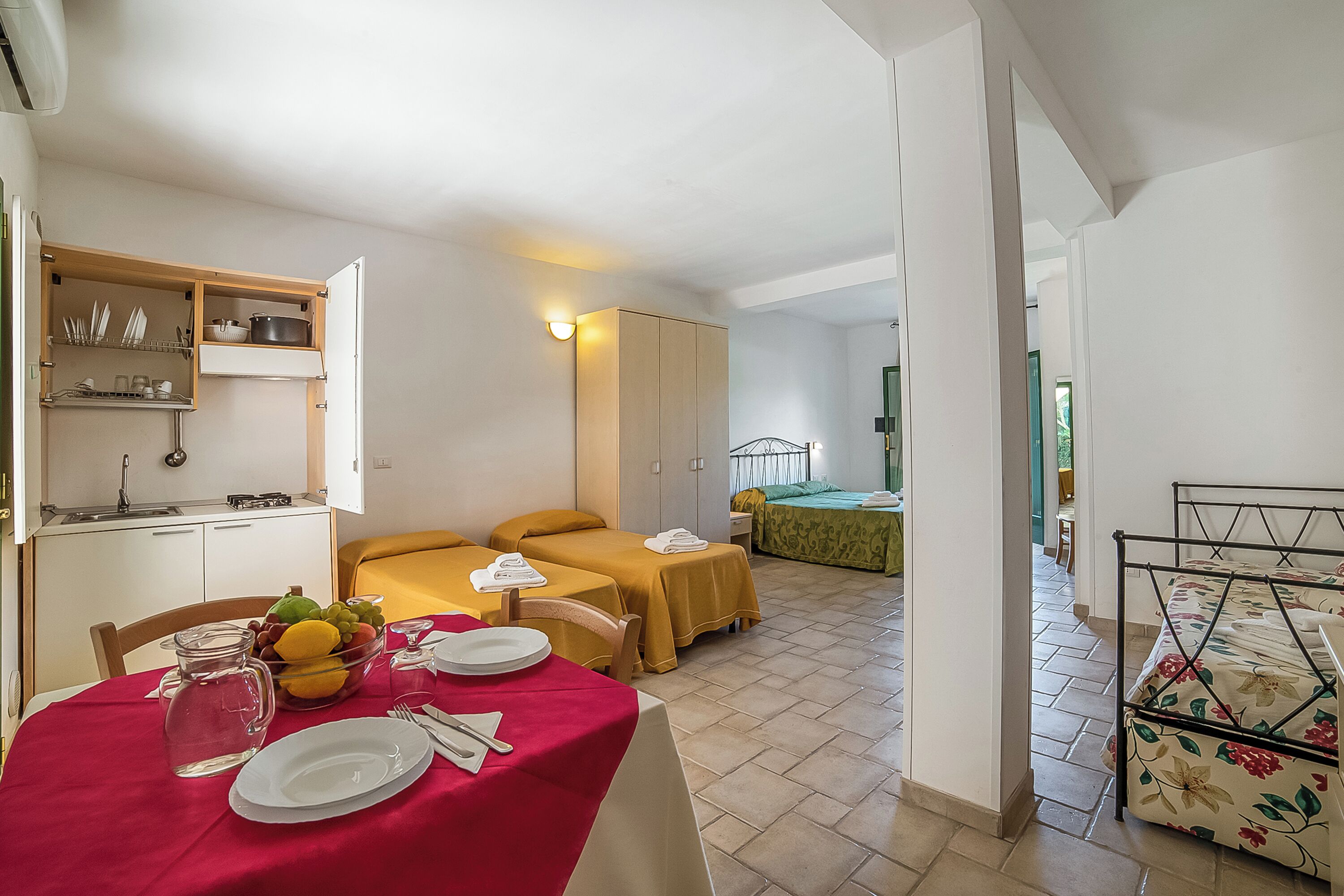A hotel room with a dining area, two beds, a kitchenette, and a view of the outside.