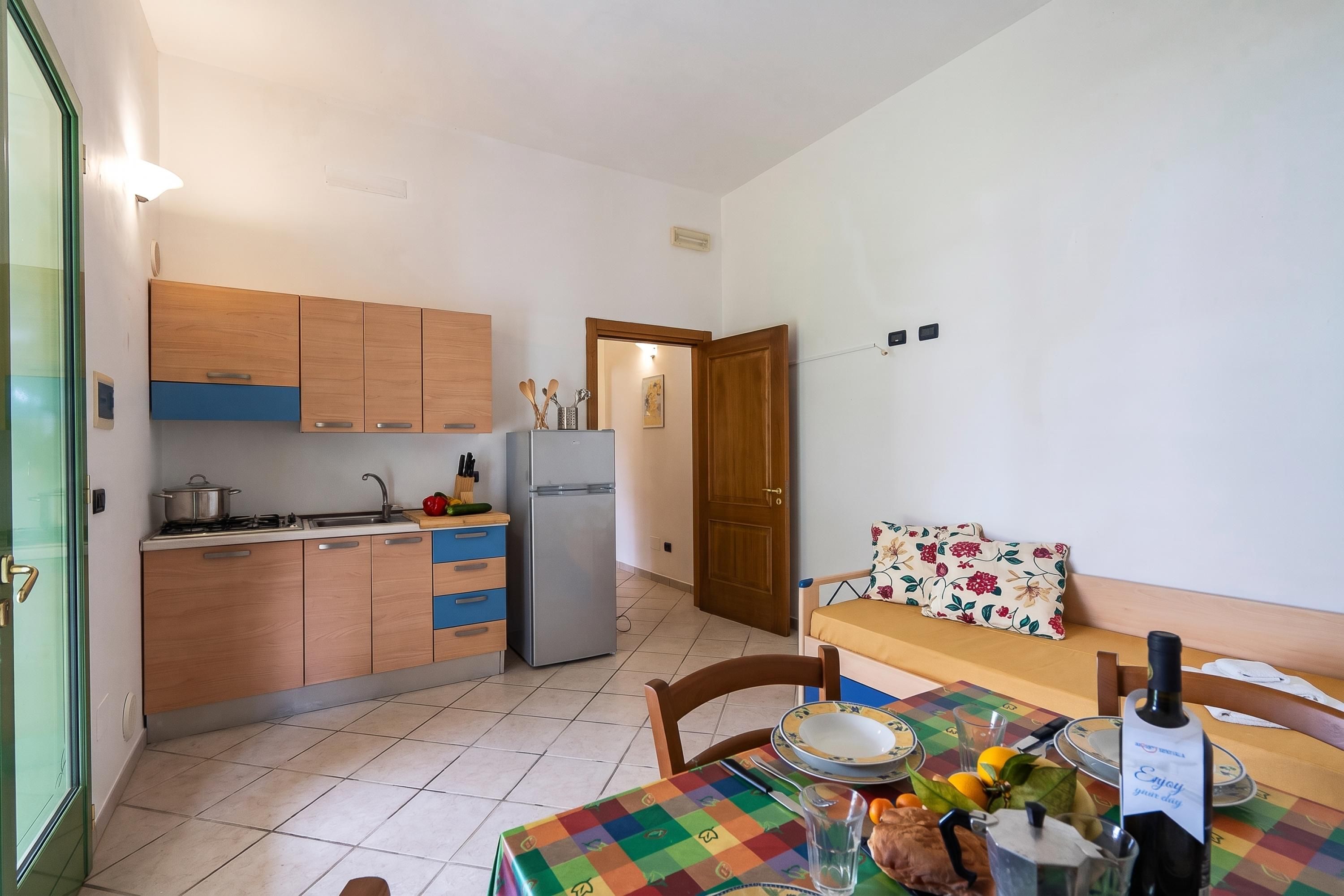 A compact kitchen with wooden cabinets, a refrigerator, and a dining area with a table set for two.