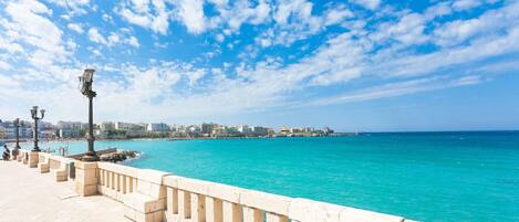 A coastal promenade with a clear view of the sea and buildings in the distance.
