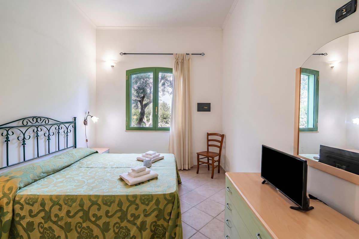 Une chambre à coucher avec un lit, une chaise, une télévision et une fenêtre avec des rideaux.