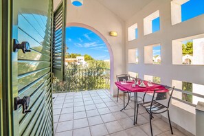 A balcony with a tiled floor, a table with chairs, and a view of buildings through a window. - Borgo Primizia Residence (Otranto)