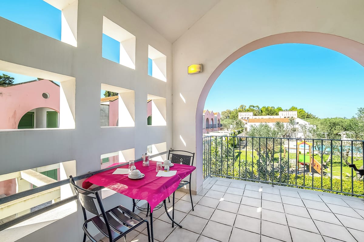 Un balcon avec une table dressée pour le dîner, une vue sur un terrain de jeux et un ciel bleu dégagé.