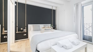 A modern bedroom with a large bed, bedside tables, a bench with towels, a blackboard, and a balcony with curtains. - Easylife - Comfort and elegance in Porta Venezia (Milano)