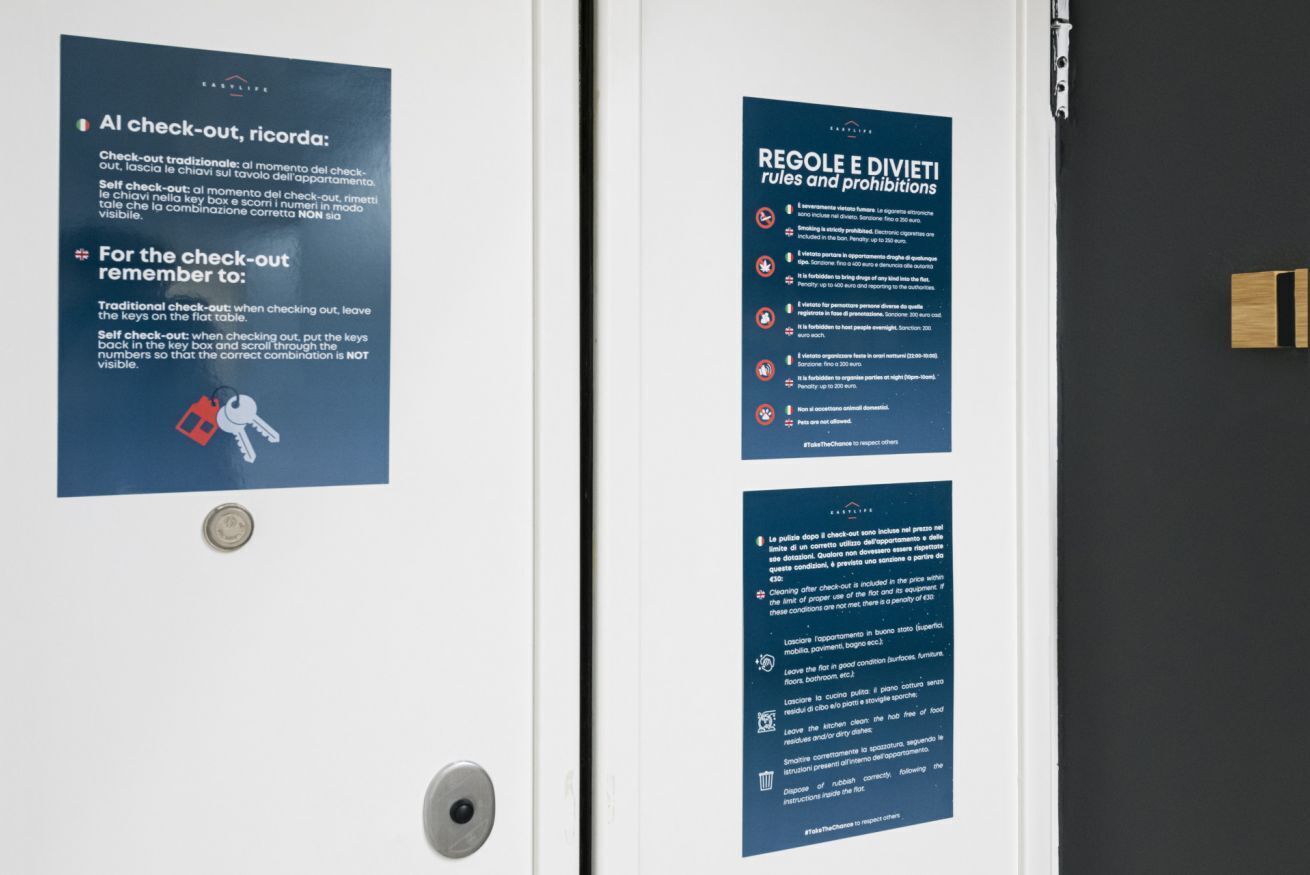 A door with two informational posters. One poster details traditional and self-check-out procedures, including instructions for handling keys. The other poster lists rules and prohibitions for the hotel, such as no smoking and no pets.
