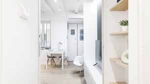 A modern, minimalist room with a flat-screen TV, white furniture, and built-in shelving with plants. - Easylife - Comfort and elegance in Porta Venezia (Milano)