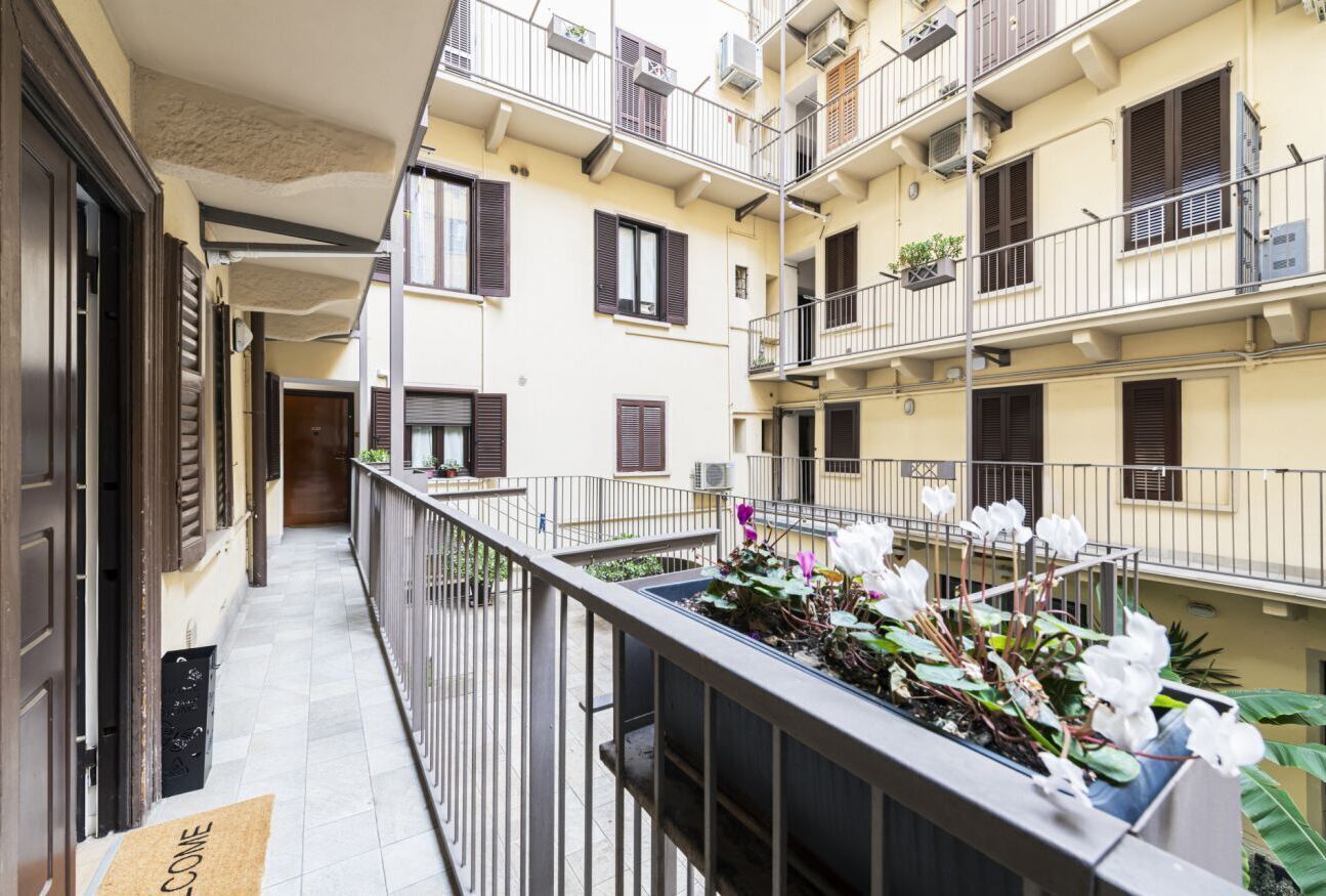 A multi-story residential building with balconies, a tiled corridor, and a doormat with "WELCOME" written on it.