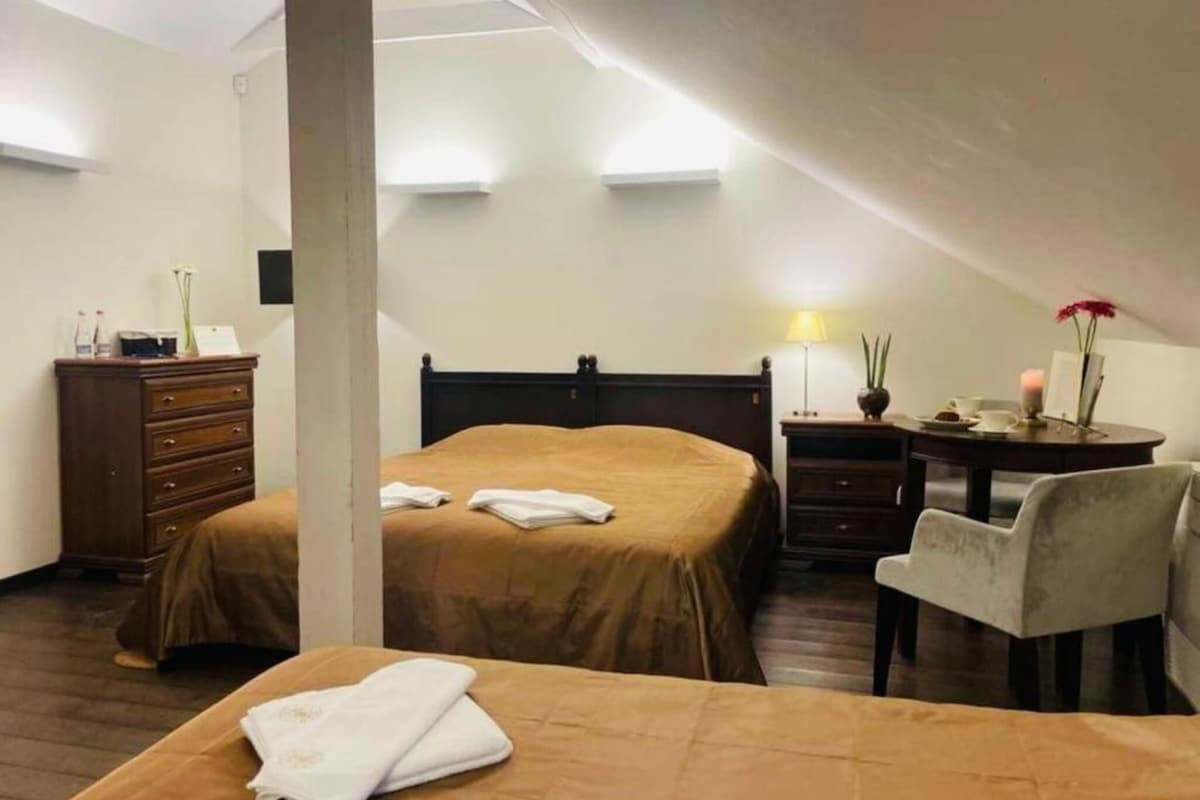A hotel room with two beds, a desk, a chair, a dresser, and a lamp.